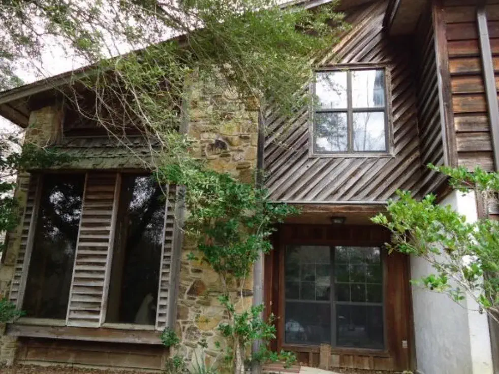 Stone chimney and weathered cedar siding of a Stonington townhome, with a vine growing across the window
