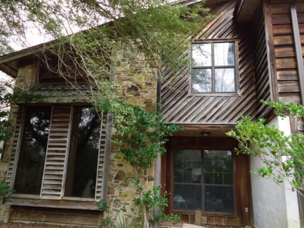 Stone chimney and weathered cedar siding of a Stonington townhome, with a vine growing across the window