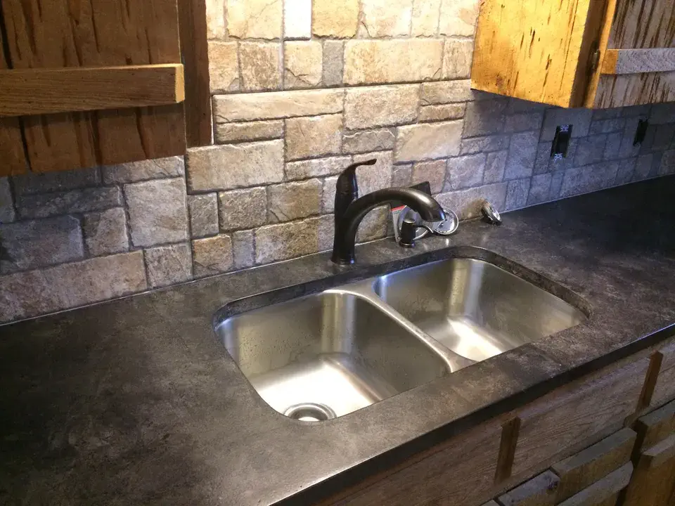 Kitchen sink with stone backsplash and wood cabinets