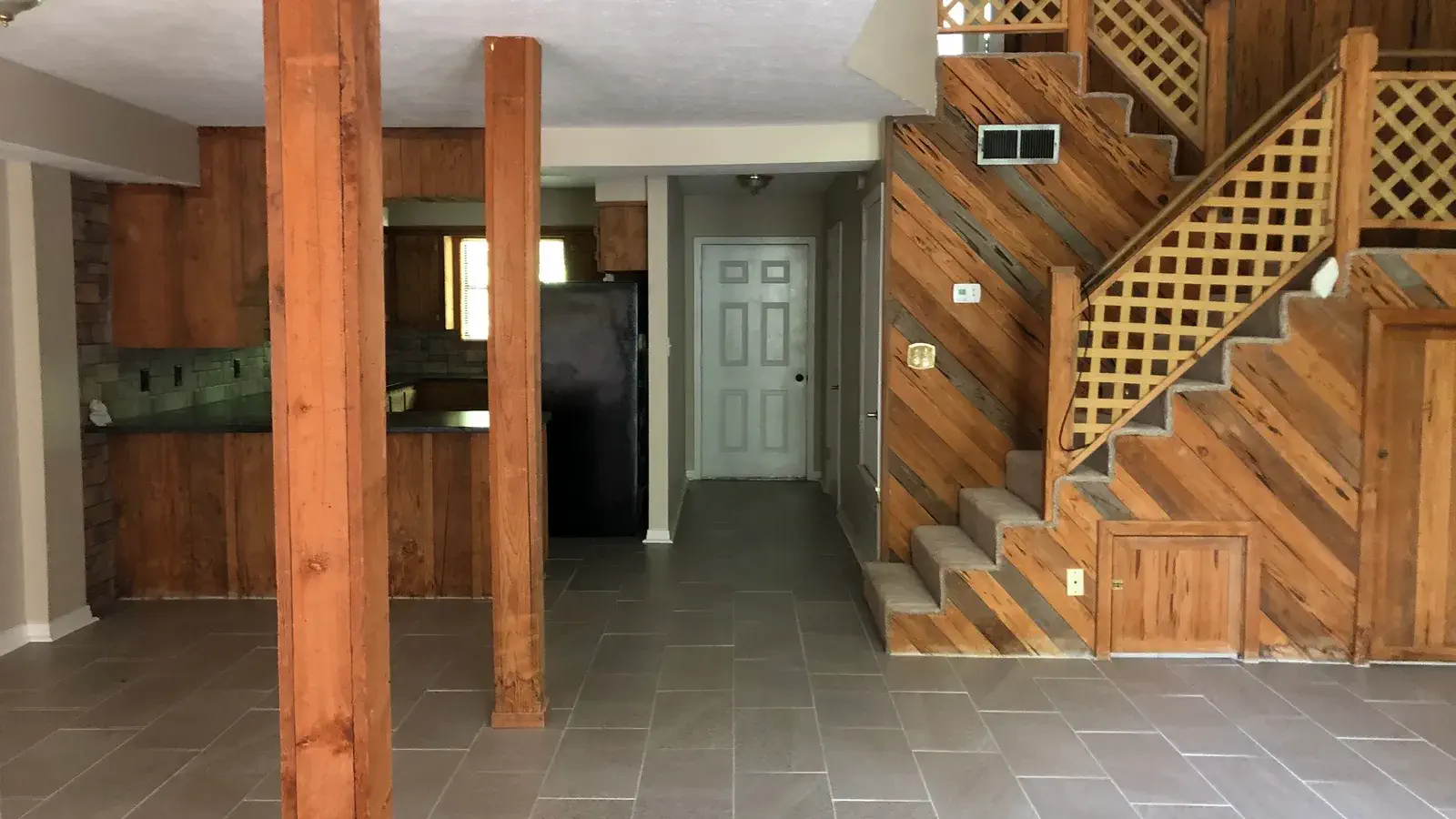 Open living area with wood columns, a lattice staircase, and the kitchen beyond