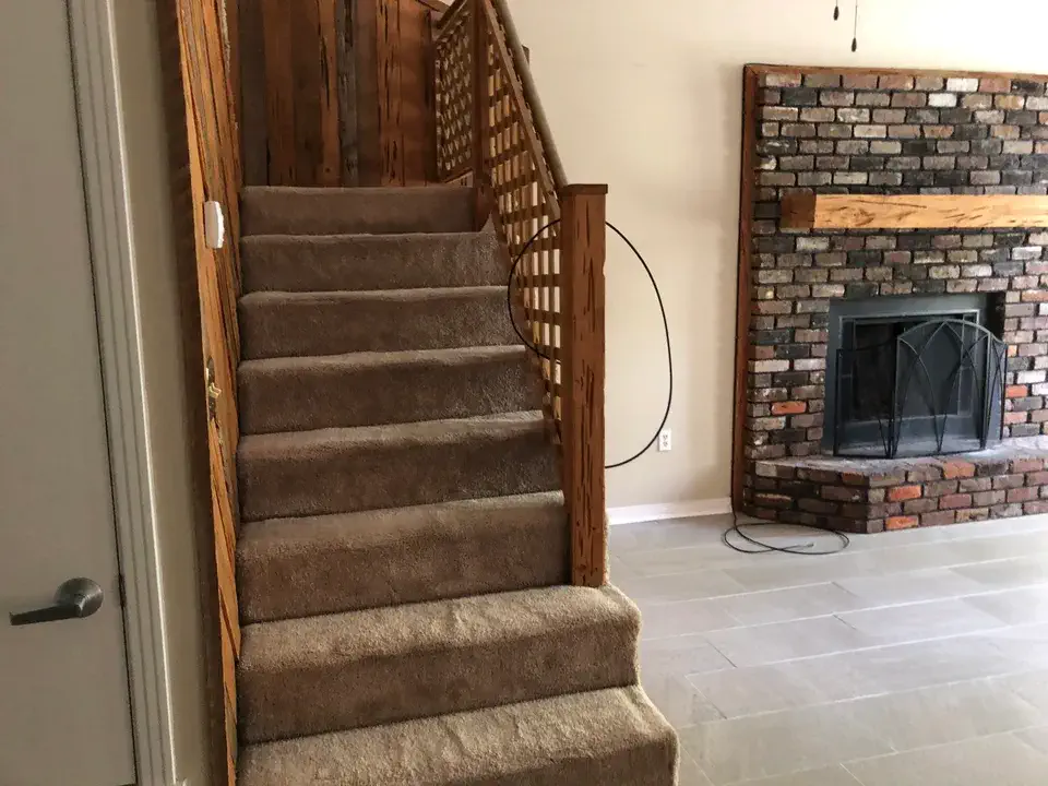 Carpeted stairs with wood railing beside the fireplace