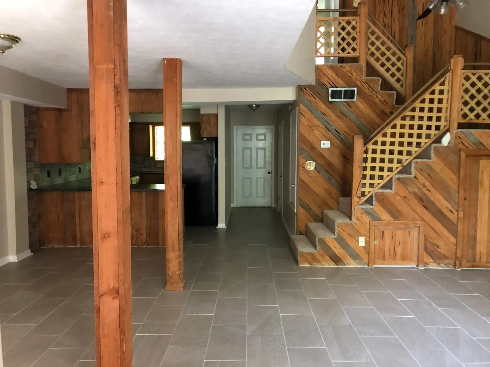 Open living area with wood columns, a lattice staircase, and the kitchen beyond
